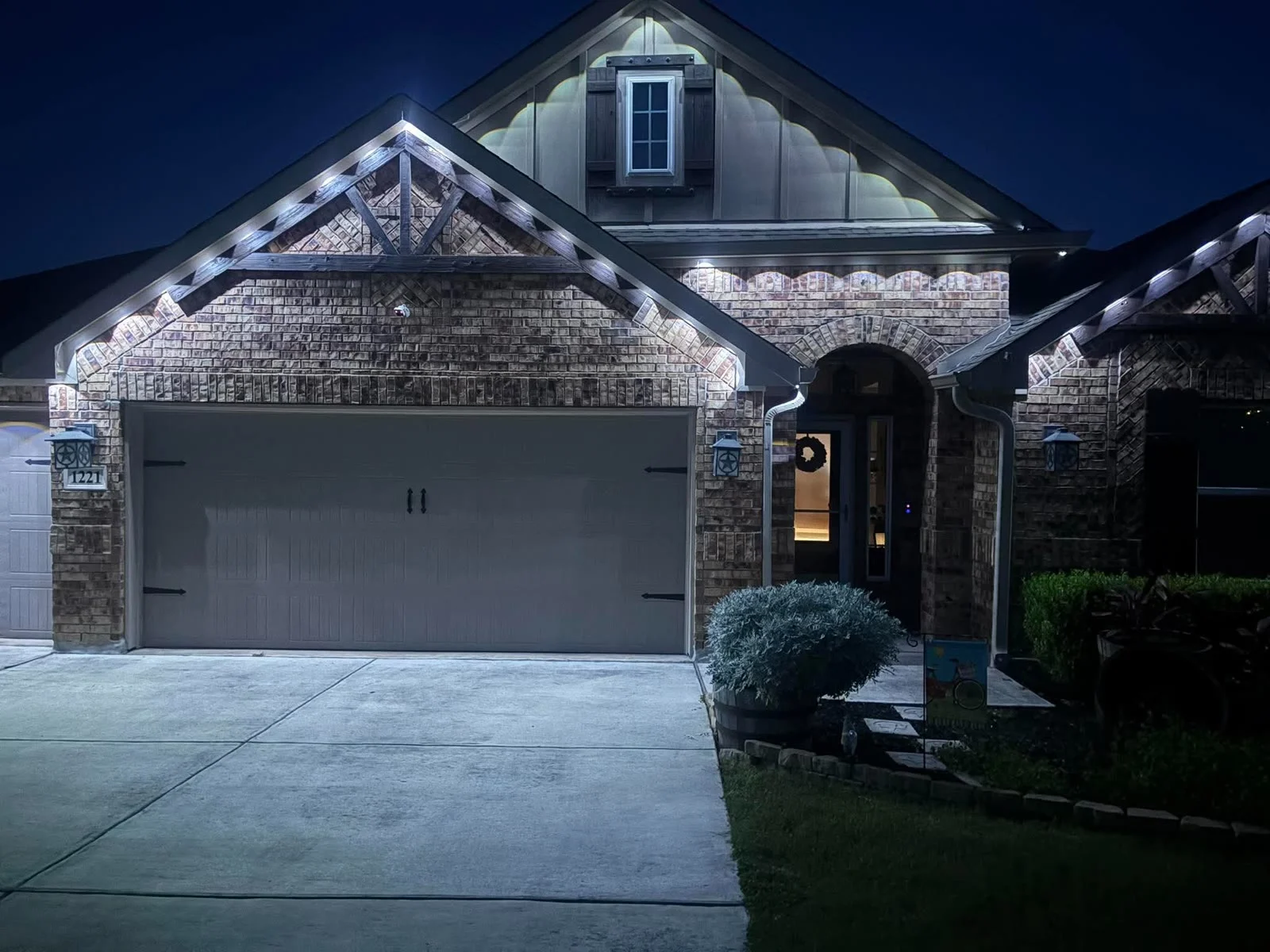 Real BrightSky install — warm-white permanent roofline lighting on a Houston brick home at night